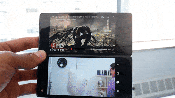 Animated GIF showing ZTE Axon M in Dual Mode with a video apps playing on each screen. The user swipes with 3 fingers to move an app from one screen to the other, and then slides 1 finger across the Android navigation bar to expand an app into Extended Mode to fill both screens.